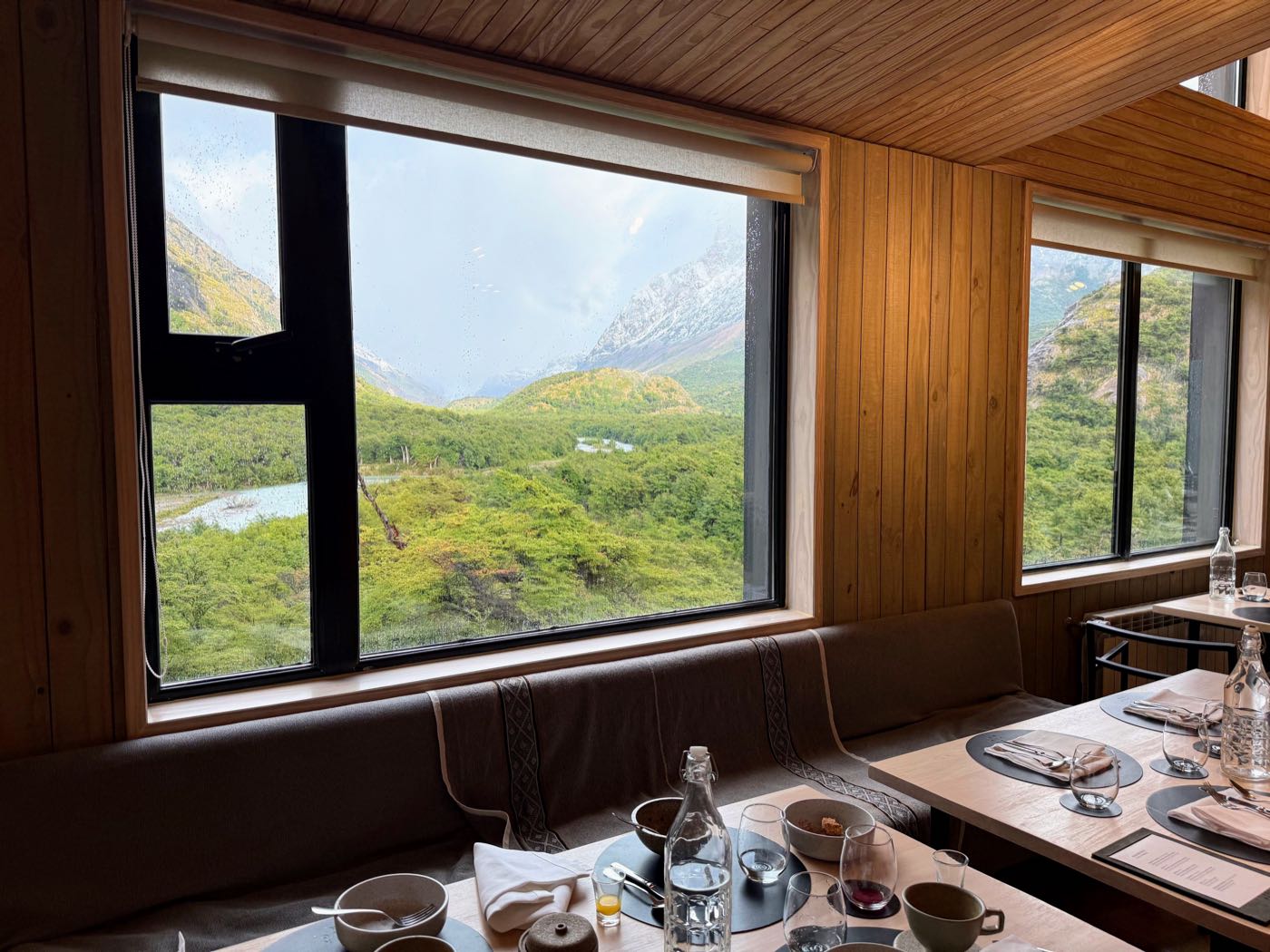 A wood-paneled dining room with big windows looking out on a green valley and mountains