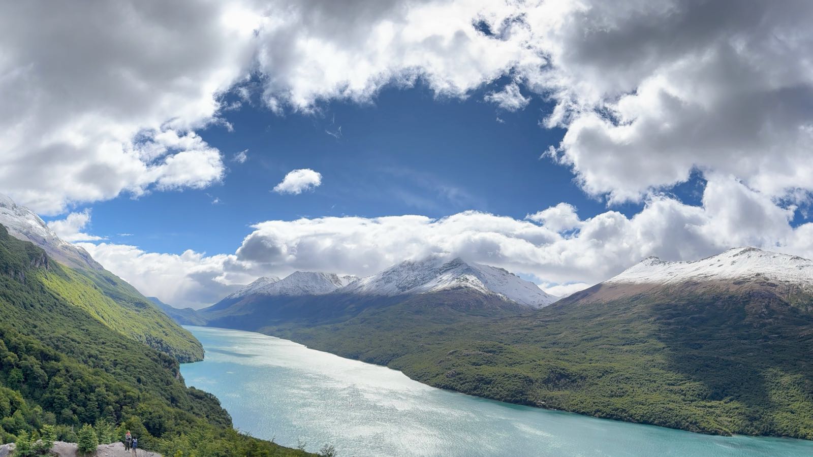 A turquoise lake between forested mountains under big clouds