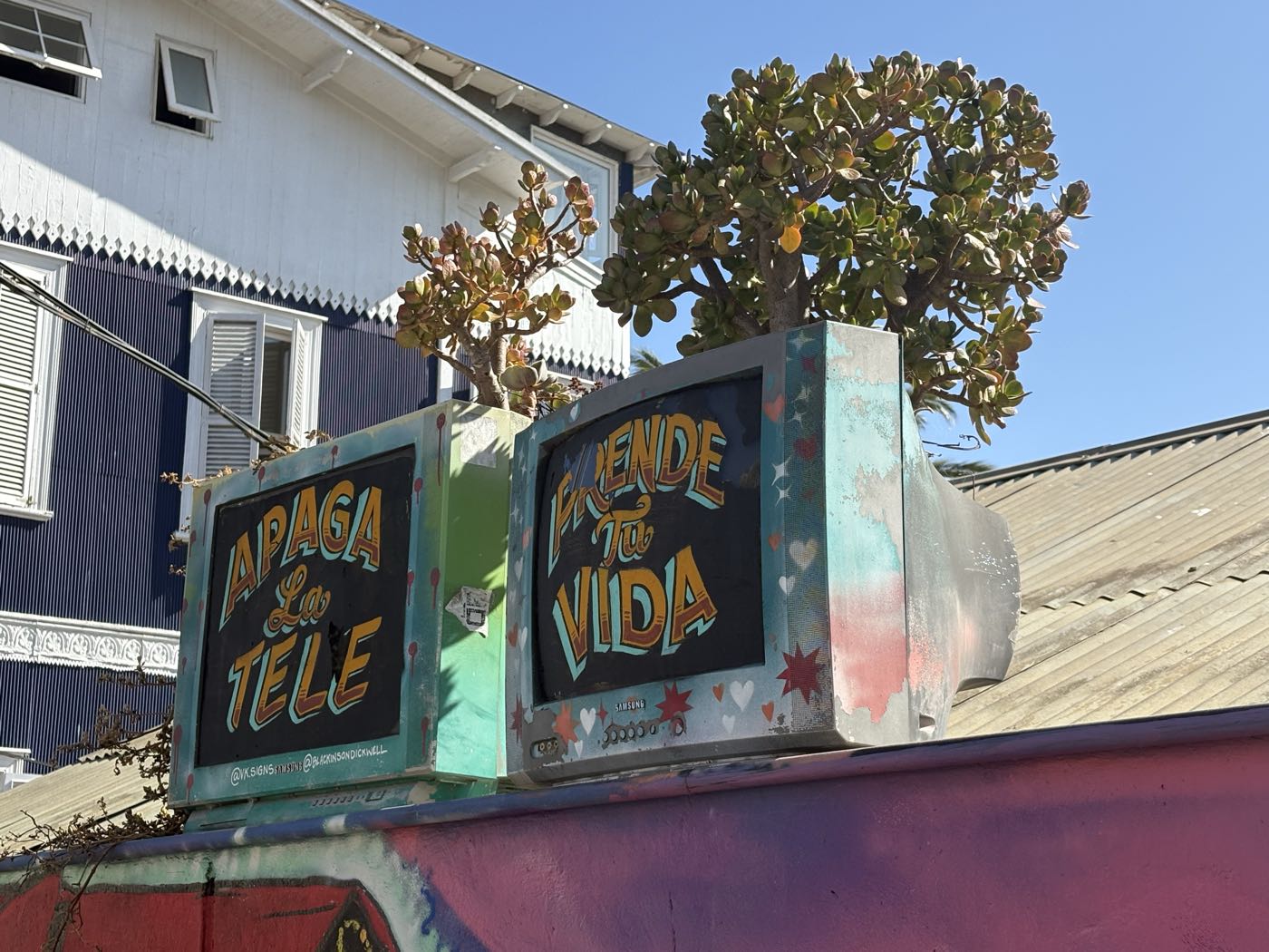 Two old TV sets used as planters, painted with the words Apaga la tele and Enciende tu vida